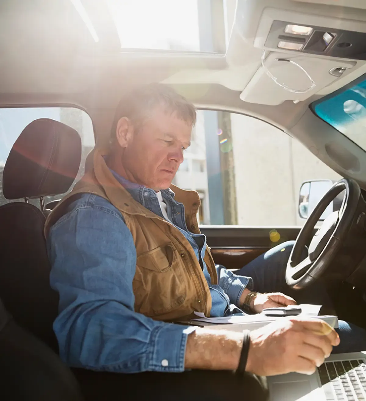 Contractor doing paperwork on a laptop in the cab of his truck