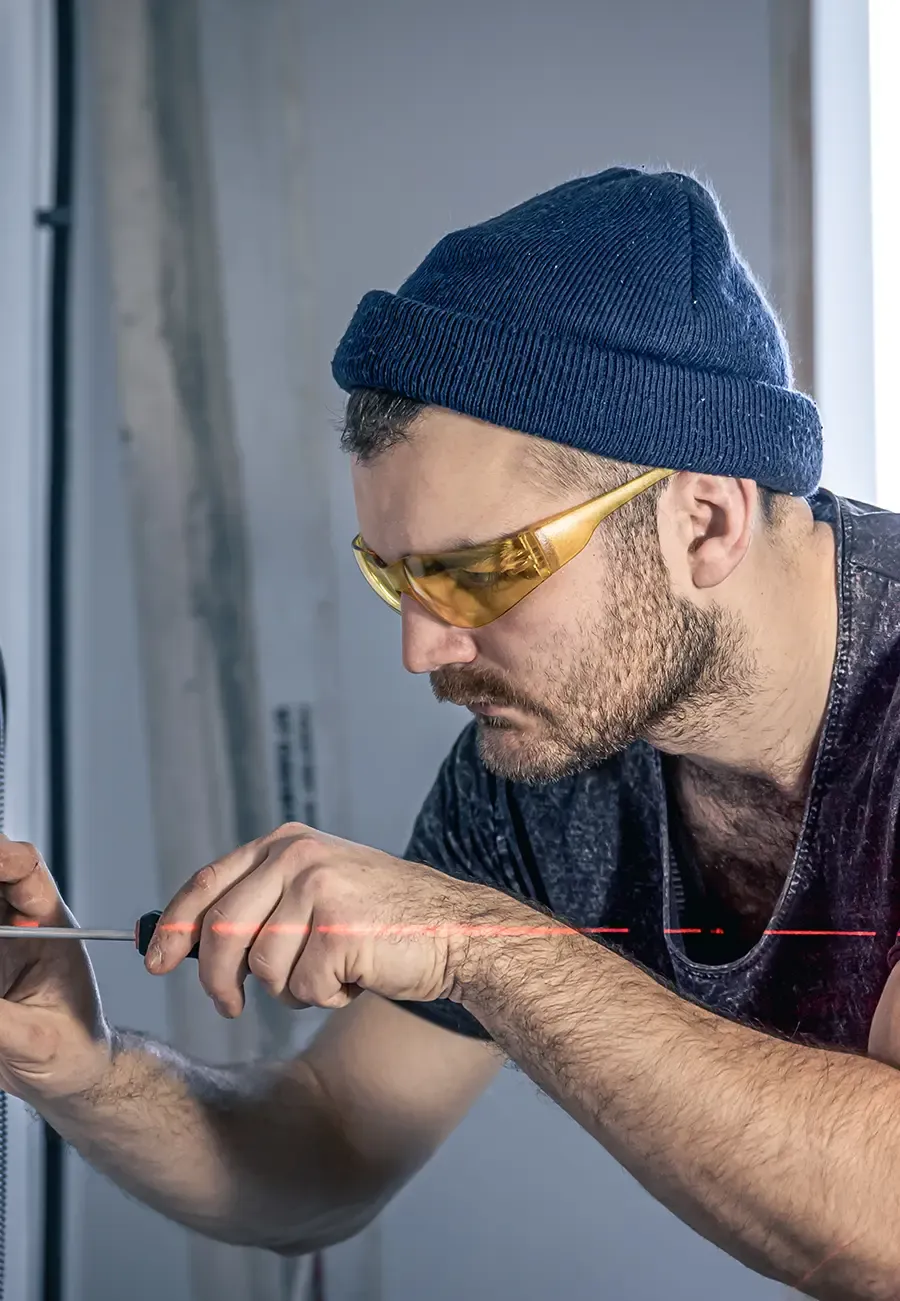 Electrician in safety glasses working on a wall panel with a screwdriver