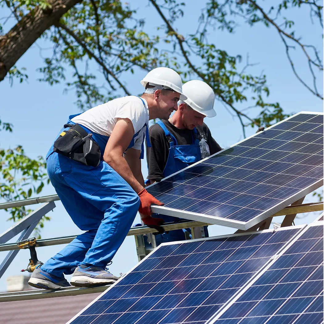 Two solar installers in hard hats setting a panel onto a roof frame