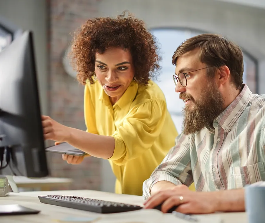 Two colleagues reviewing figures together on a desktop monitor
