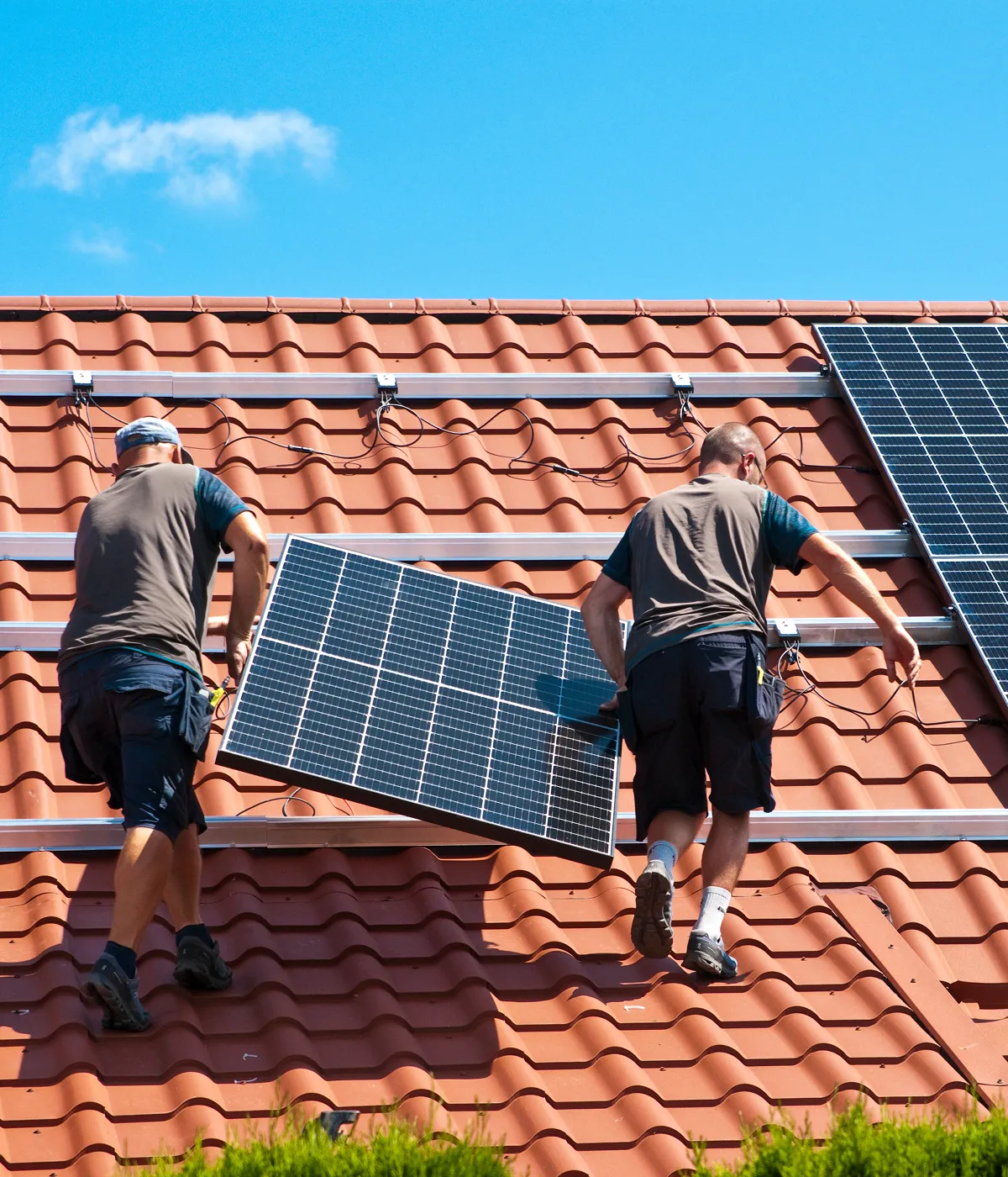 Two installers carrying a solar panel across a tiled roof