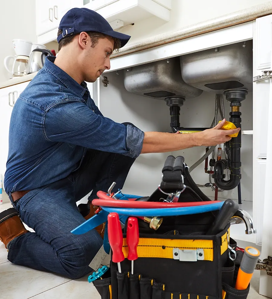Plumber kneeling to work on the pipework under a kitchen sink