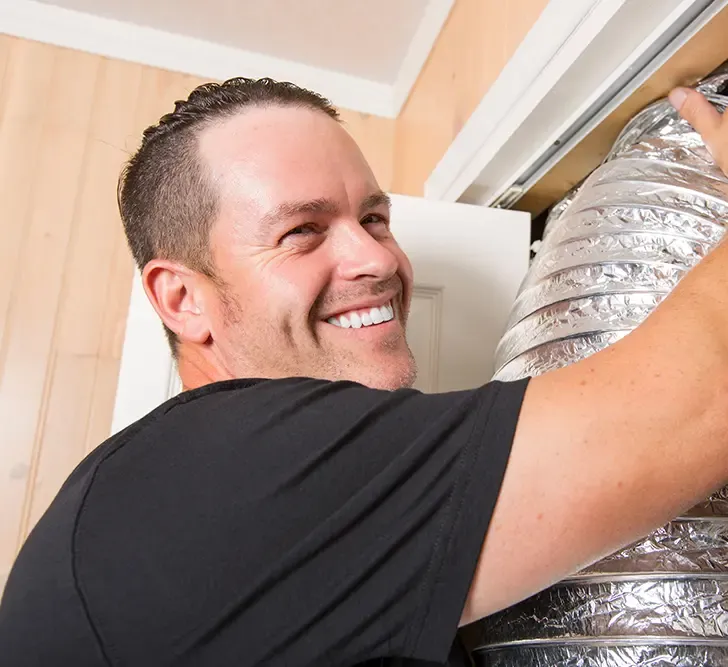 HVAC technician smiling as he connects a length of flexible ductwork